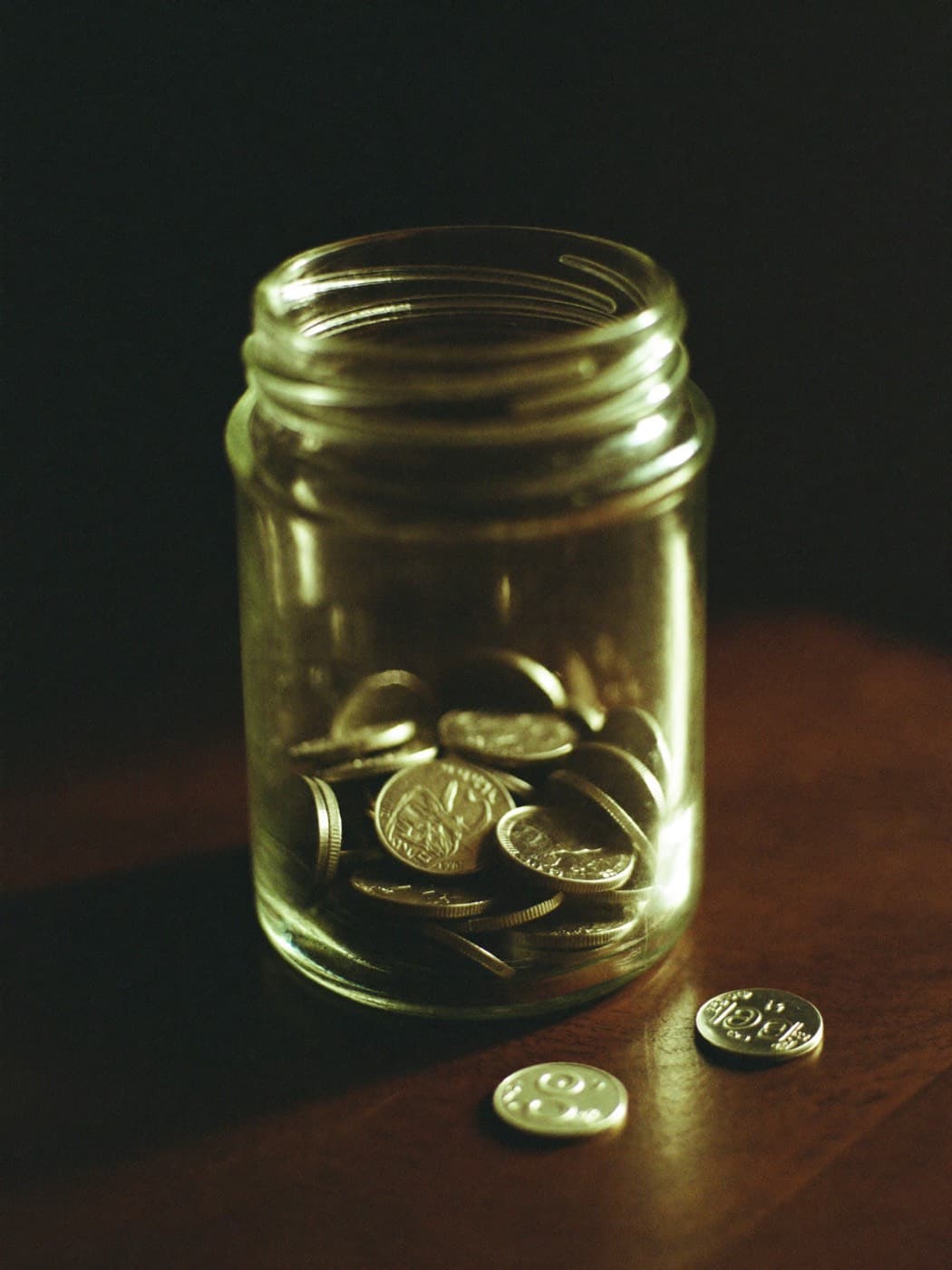 Pote de vidro com moedas sobre uma mesa escura