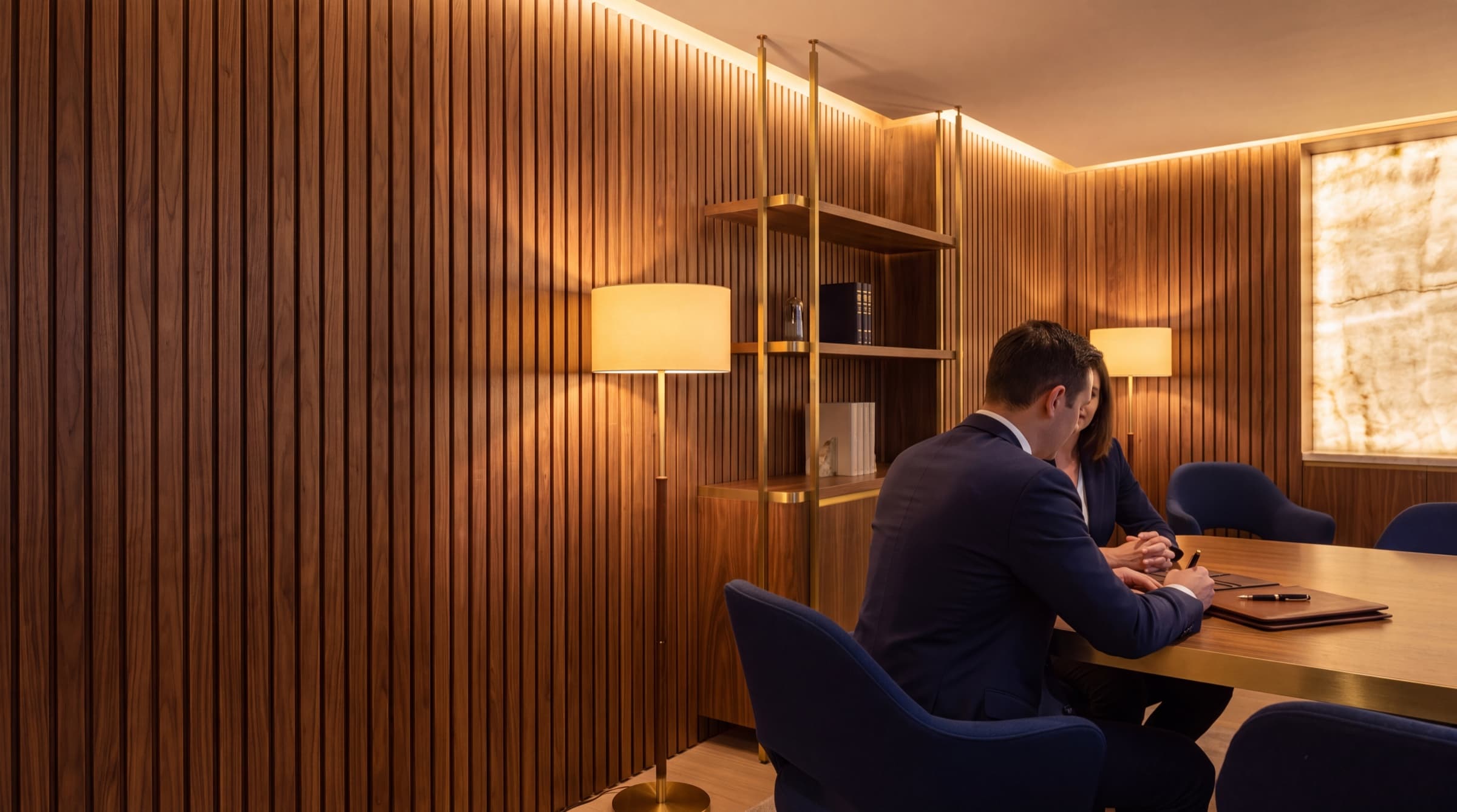 Planejador de terno em reunião com uma cliente à mesa de uma sala revestida de madeira ripada